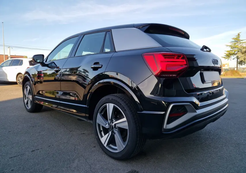 Audi Q2 noir vue 3/4 arrière droit, avec toit contrastant gris et feux arrière LED distinctifs.