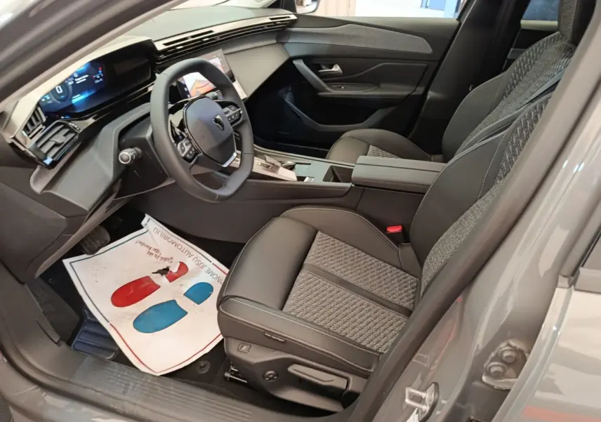 Vue intérieure côté conducteur de la Peugeot 308 gris foncé, volant cuir multifonctions et sièges tissu-cuir bicolores.