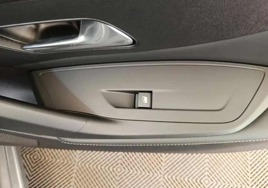 Détail de la commande de lève-vitre côté conducteur sur la porte intérieure d'une Peugeot 308 gris foncé 2026.