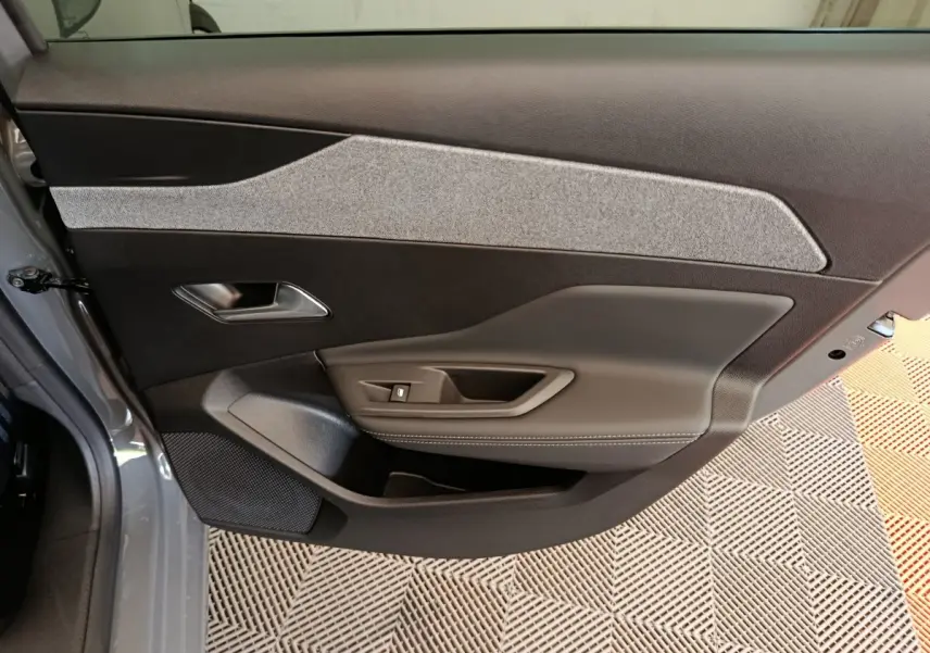 Vue intérieure de la porte avant gauche de la Peugeot 308 gris foncé, avec garniture tissu et commandes de fenêtre.