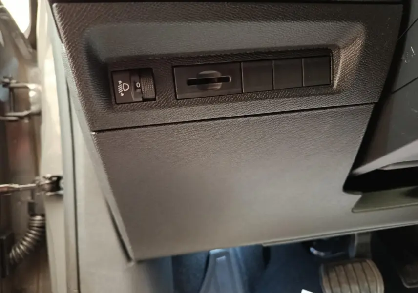 Vue intérieure côté conducteur de la Peugeot 308 gris foncé, avec commandes d'éclairage et pédales visibles.