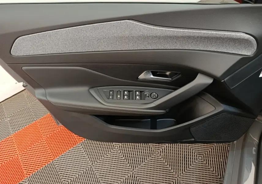 Vue intérieure côté gauche de la porte avant d'une Peugeot 308 gris foncé avec commandes de vitres et poignée métallique.