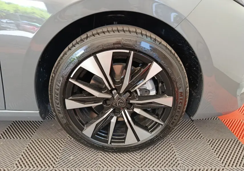 Gros plan sur la roue avant droite d’une Peugeot 308 gris foncé, jante alliage noir et argentée au design moderne.