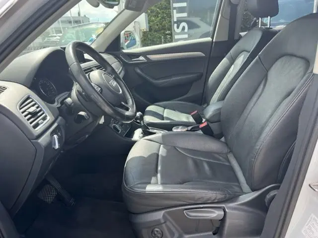 Intérieur côté conducteur de l'Audi Q3 blanc 2015, montrant sièges cuir noirs et tableau de bord moderne.