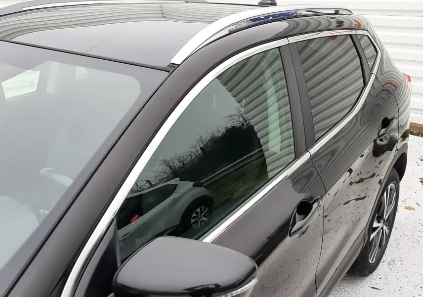 Vue de profil avant droit du Nissan Qashqai noir 2020, mettant en valeur la finition brillante et les barres de toit argentées.