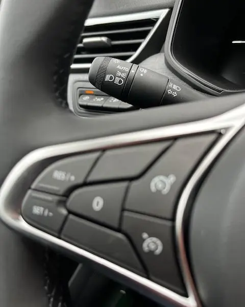 Gros plan sur les commandes au volant et la manette des phares d'une Renault Clio noire, intérieur moderne avec finitions chromées.