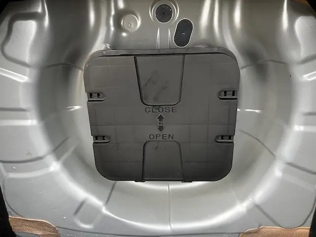 Détail du compartiment de rangement sous le plancher du coffre d'une Renault Clio noire, vue de dessus.