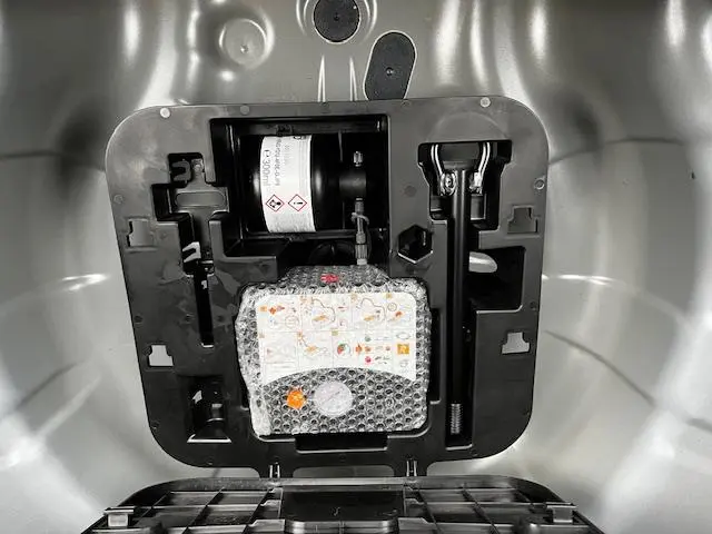 Vue rapprochée du coffre d'une Renault Clio noire 2025 montrant le kit de réparation pneu et les outils de bord.