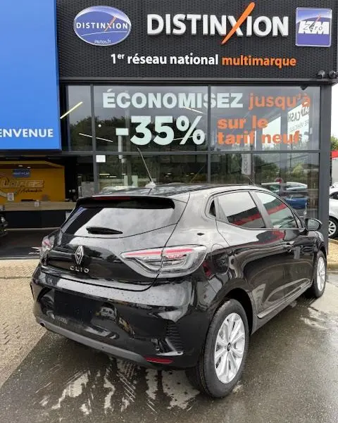Vue 3/4 arrière droite d'une Renault Clio noire Evolution Blue dCi 100, stationnée devant un concessionnaire multimarque.