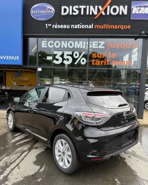 Renault Clio noire vue en 3/4 arrière droit, avec feux LED et jantes alliage, devant une vitrine commerciale.