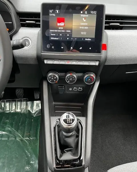 Vue intérieure centrée sur la console centrale d'une Renault Clio noire 2025, avec écran tactile et levier de vitesse manuel.
