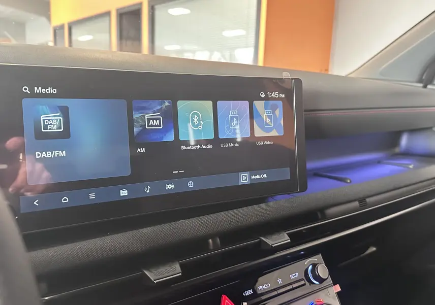 Gros plan sur les commandes noires du volant perforé avec surpiqûres rouges du Hyundai Tucson 2025 hybride.