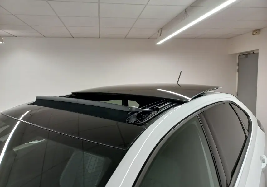 Vue rapprochée du toit ouvrant ouvert sur le côté gauche d’un Volkswagen Taigo blanc pur 2025 en intérieur.