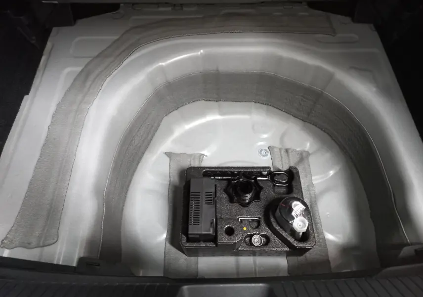 Vue en plongée sur le coffre ouvert d’un Volkswagen Taigo blanc pur 2025, montrant le rangement sous plancher avec kit de réparation pneus.