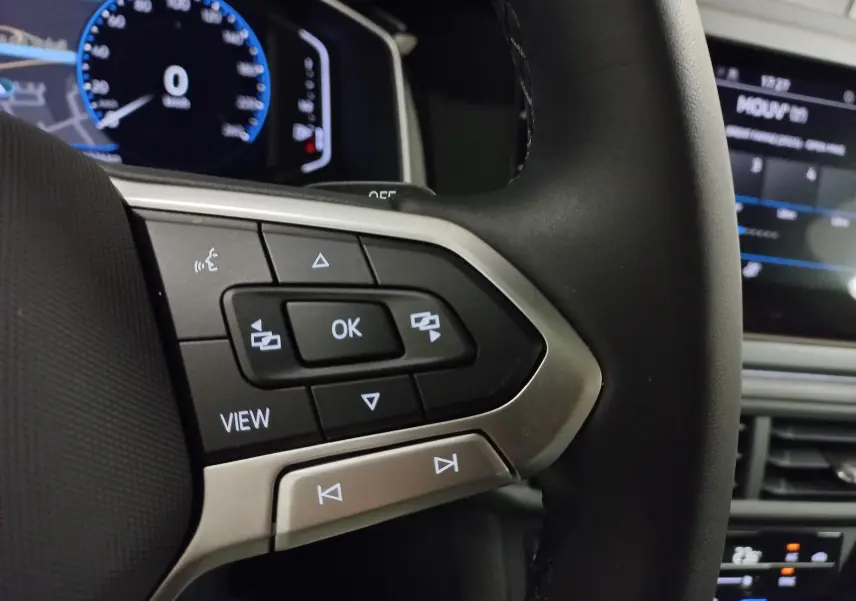 Gros plan sur les commandes au volant à gauche du Volkswagen Taigo blanc pur 2025, avec tableau de bord numérique en arrière-plan.