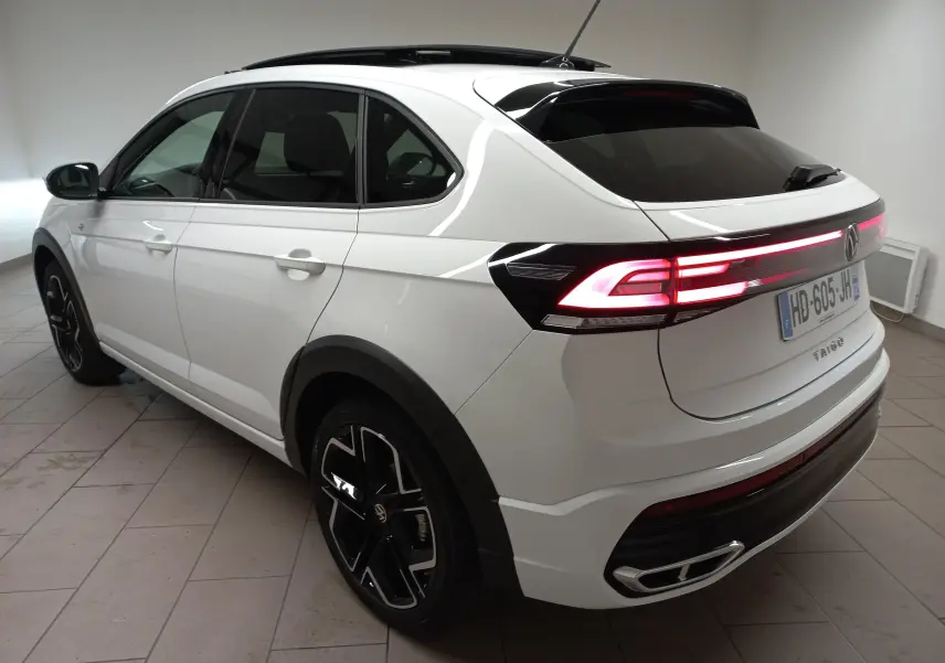 Volkswagen Taigo blanc pur en 3/4 arrière droit, feux arrière allumés et toit ouvrant visible.