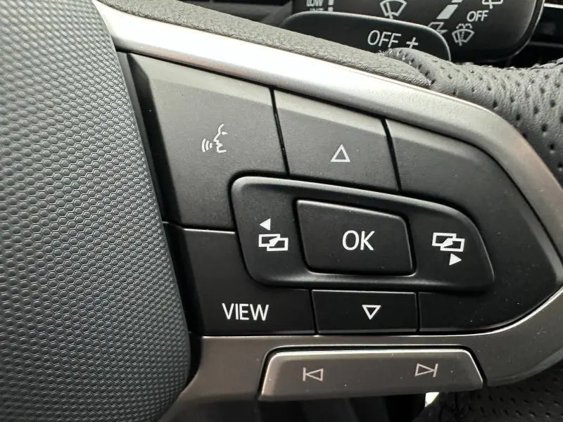 Gros plan sur les commandes multifonctions noires du volant cuir du Volkswagen T-Roc gris, avec bouton OK et flèches.