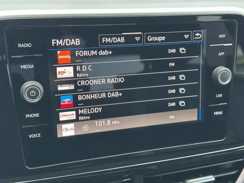 Écran tactile central du Volkswagen T-Roc gris, affichant les stations radio FM/DAB avec commandes latérales.