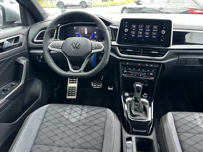 Vue intérieure du tableau de bord et volant cuir multifonctions du Volkswagen T-Roc gris, avec écran tactile central et levier de boîte auto.