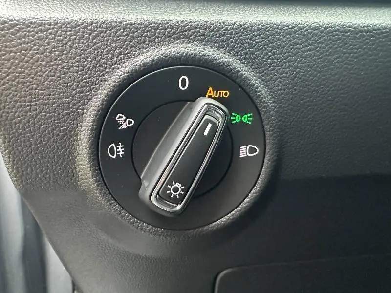 Gros plan sur le sélecteur de phares noir avec fonction automatique dans l'habitacle gris du Volkswagen T-Roc 2025.