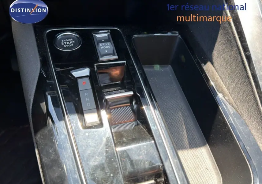 Gros plan sur la console centrale noire brillante du Peugeot 3008 Hybrid 2024 avec sélecteur de vitesse et bouton start/stop.