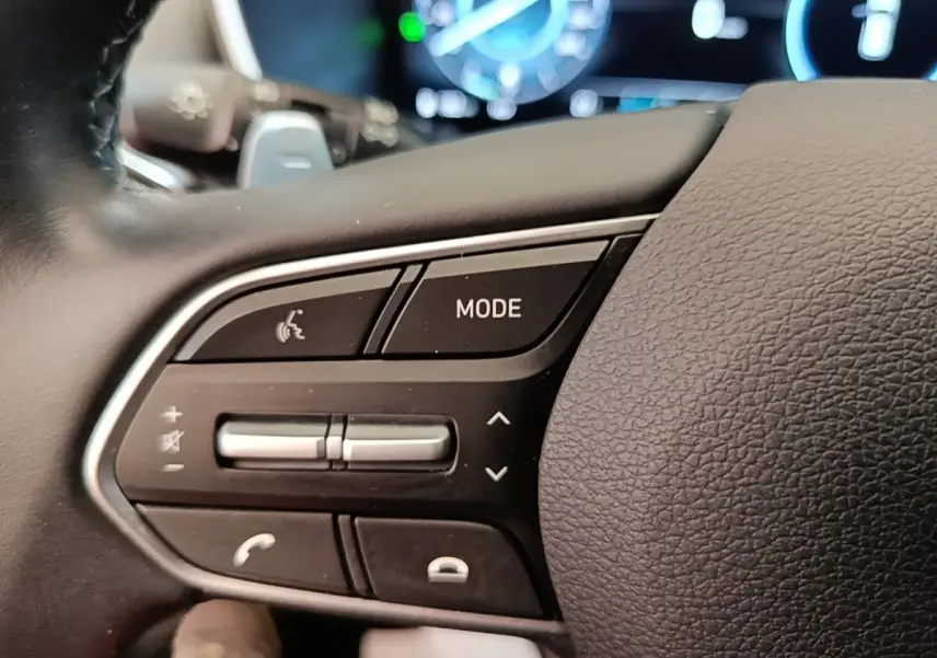 Gros plan sur les commandes gauche du volant cuir du Hyundai Santa Fe 2023, avec touches mode et volume.