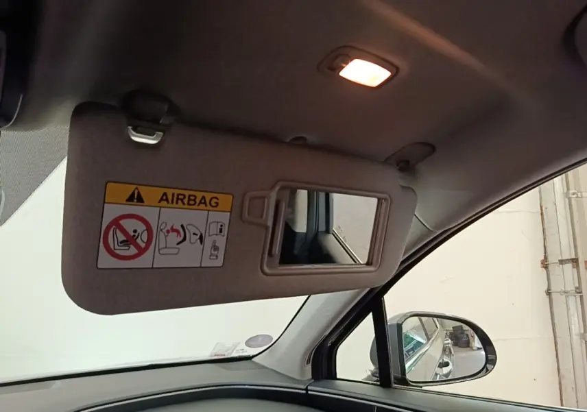 Détail intérieur du pare-soleil côté conducteur avec miroir et avertissement airbag, éclairage allumé, vue vers la portière noire.