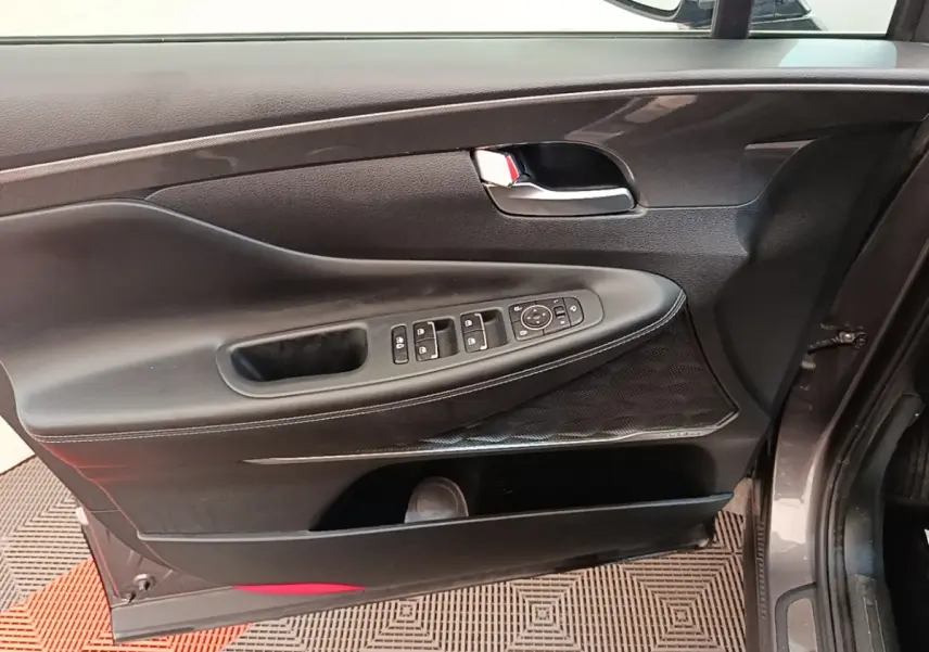 Vue intérieure de la porte avant gauche du Hyundai Santa Fe gris foncé, avec commandes électriques et poignée chromée.