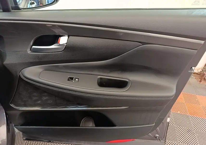 Vue rapprochée de la porte intérieure côté gauche d’un Hyundai Santa Fe gris foncé avec garniture noire et poignée chromée.