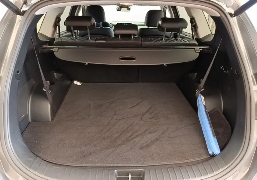 Vue intérieure du coffre ouvert du Hyundai Santa Fe gris foncé, montrant la tablette cache-bagages et les sièges arrière rabattables.