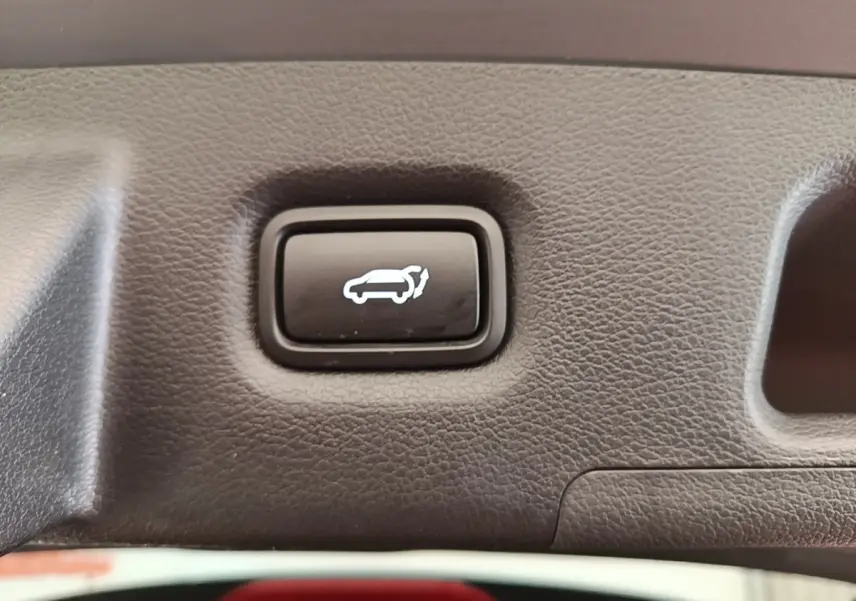 Bouton noir d'ouverture électrique du coffre sur panneau intérieur gris texturé du Hyundai Santa Fe 2023.