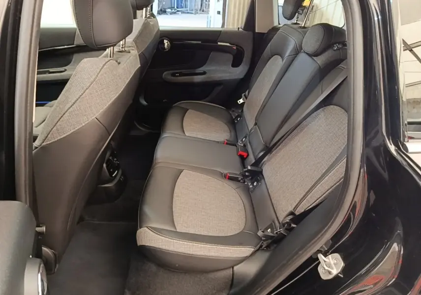 Vue côté gauche sur l'intérieur arrière du MINI Countryman noir 2023, sièges tissu et cuir bicolores avec ceinture grise.