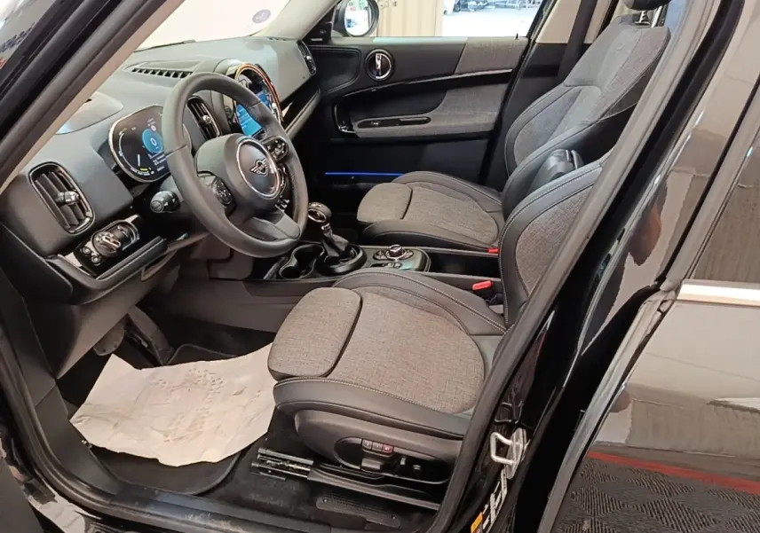 Vue intérieure côté conducteur du MINI Countryman noir 2023, sièges tissu gris et volant cuir multifonctions.