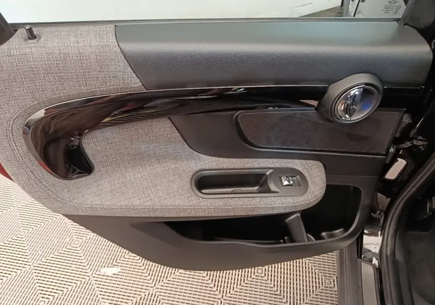 Gros plan sur la porte intérieure côté gauche de la MINI Countryman noire, avec habillage tissu gris et poignée noire brillante.