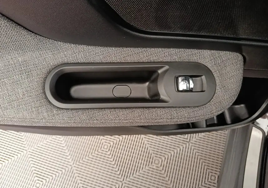 Poignée intérieure de porte côté gauche du MINI Countryman noir, avec revêtement tissu gris et bouton chromé.