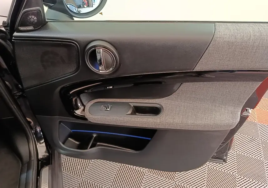 Intérieur de la porte avant gauche noire du MINI Countryman 2023 avec habillage tissu gris et éclairage d’ambiance bleu.