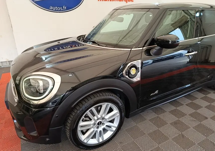 Vue 3/4 avant droit d'une MINI Countryman hybride noire avec jantes argentées et logo électrique sur l'aile.