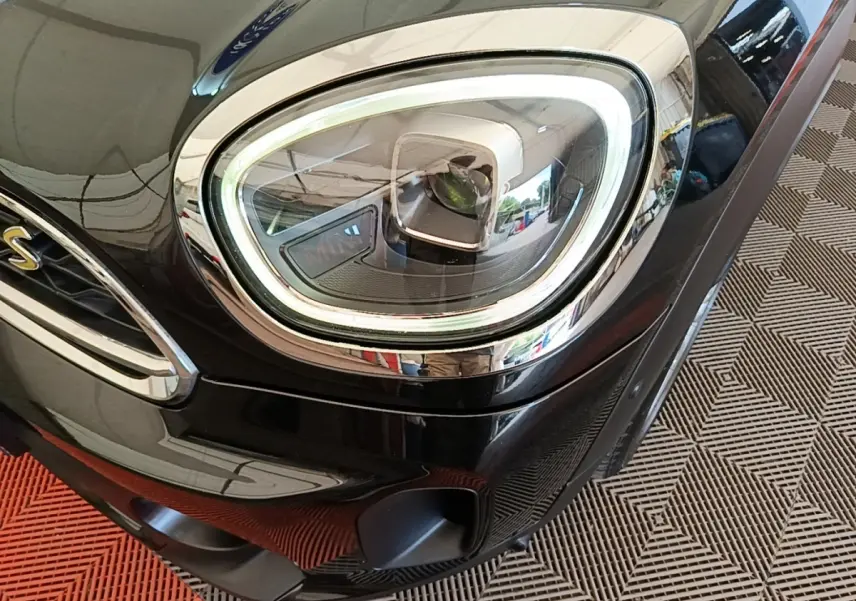 Gros plan sur le phare avant droit LED d'une MINI Countryman Cooper SE noire, avec calandre et logo "S" visibles.