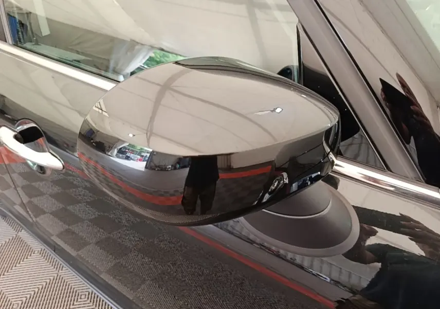 Gros plan sur le rétroviseur droit noir brillant du MINI COUNTRYMAN Cooper SE 2023, reflétant l'environnement intérieur.