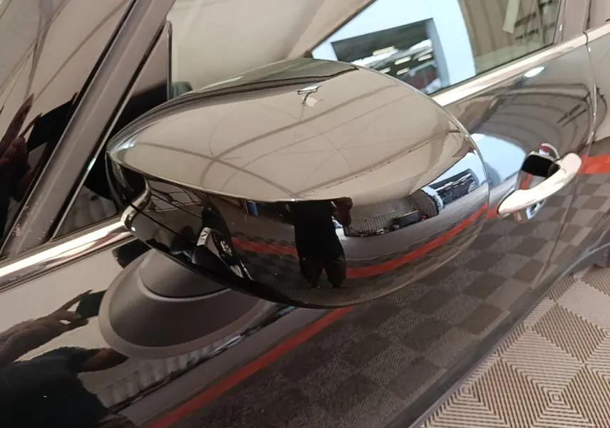 Gros plan sur le rétroviseur droit noir brillant d'un MINI Countryman 2023, reflet de l'environnement intérieur visible.