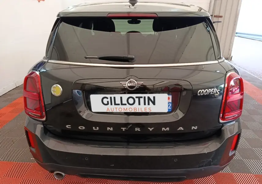 Vue arrière d'une MINI Countryman Cooper SE noire avec logo hybride jaune sur le côté gauche du coffre.