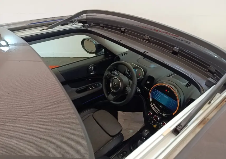 Vue intérieure du MINI Countryman Cooper SE 2023 noir, toit ouvrant électrique ouvert, tableau de bord et volant cuir visibles.
