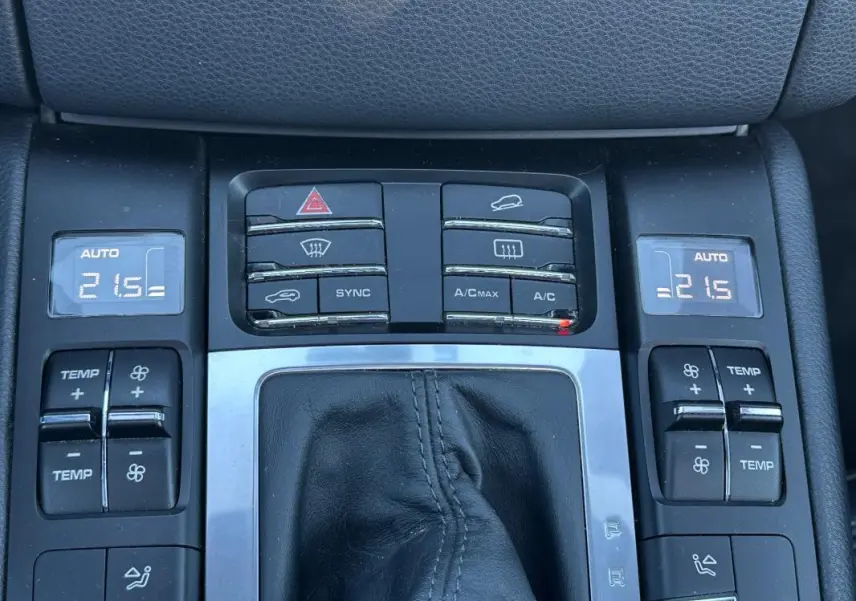 Vue rapprochée de la console centrale du Porsche Macan gris foncé, montrant les commandes de climatisation automatique et les boutons de réglage.
