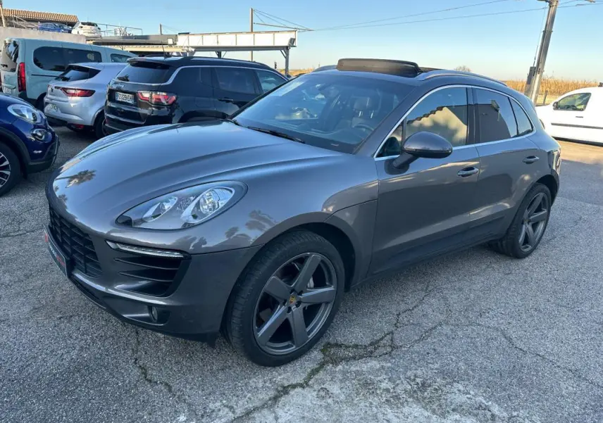 Porsche Macan gris foncé vue 3/4 avant droit, jantes 18 pouces, vitres teintées et toit panoramique visible.