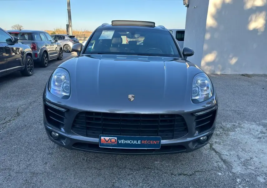 Vue avant d'un Porsche Macan gris foncé 2015 avec toit panoramique et calandre noire, stationné en extérieur.