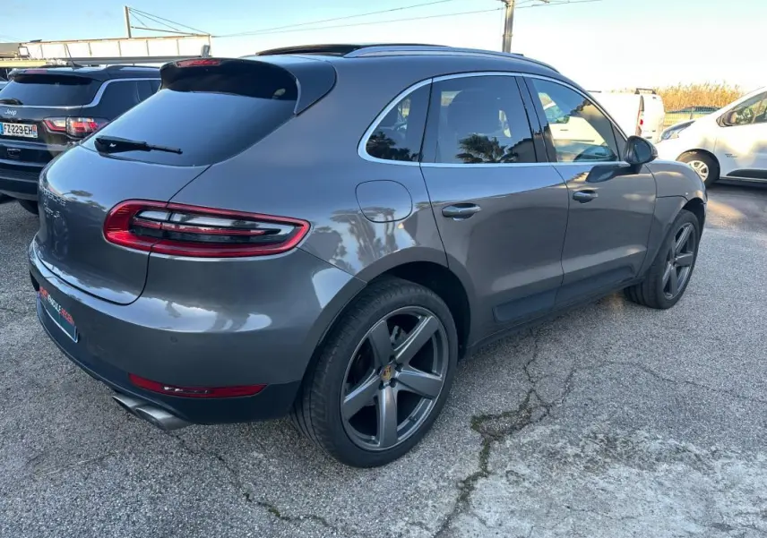 Vue 3/4 arrière droite d'un Porsche Macan gris foncé avec jantes 18 pouces et toit panoramique visible.