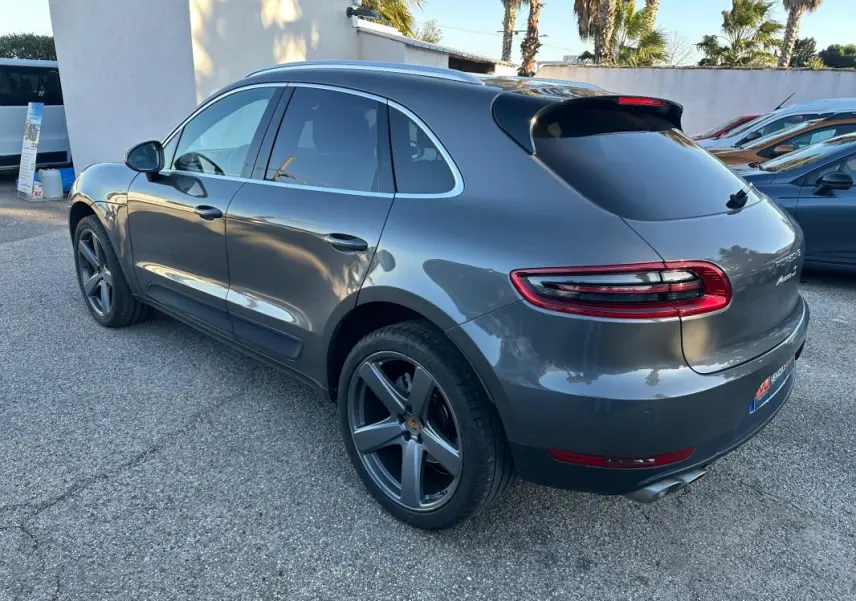 Vue 3/4 arrière droite d'un Porsche Macan gris foncé avec jantes 18 pouces et vitres teintées.