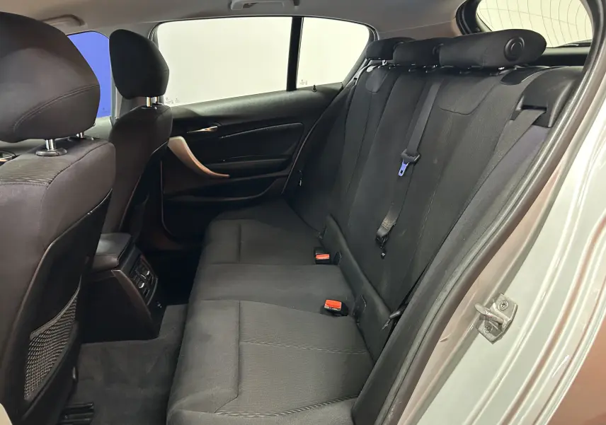Vue intérieure arrière côté droit de la BMW Série 1 gris, montrant les sièges en tissu noir et les appuie-têtes.
