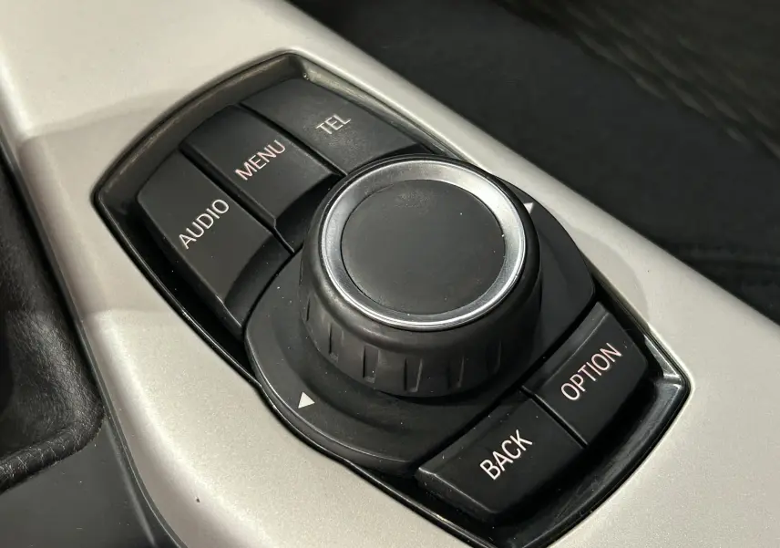 Gros plan sur la molette de commande centrale noire entourée de boutons AUDIO, MENU, TEL, BACK et OPTION sur console argentée d'une BMW Série 1.