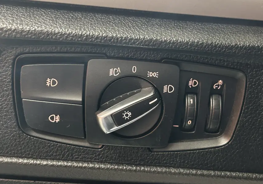 Gros plan sur le panneau de commande des phares et réglages lumineux intérieur noir d'une BMW Série 1 16d 2014.